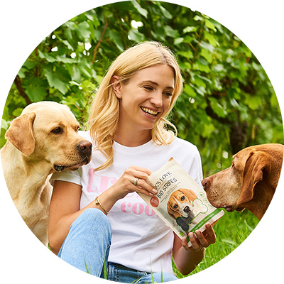 Katharina Miklauz mit Pluto und Enzo zwischen Reben füttert DOG'S LOVE Hundesnacks