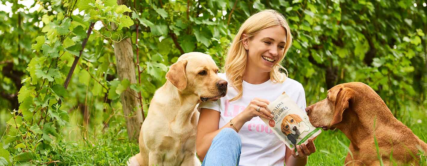 Katharina Miklauz sits among the vines feeding the dogs Enzo and Pluto with our DOG'S LOVE Snacks
