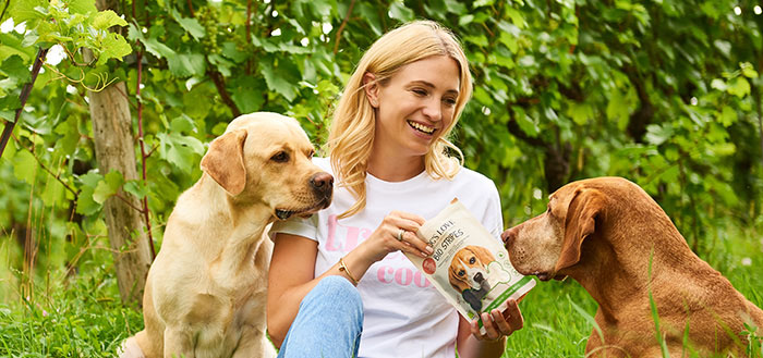 Katharina Miklauz sentada entre las viñas dando de comer a los perros Enzo y Pluto con nuestros DOG'S LOVE Snacks